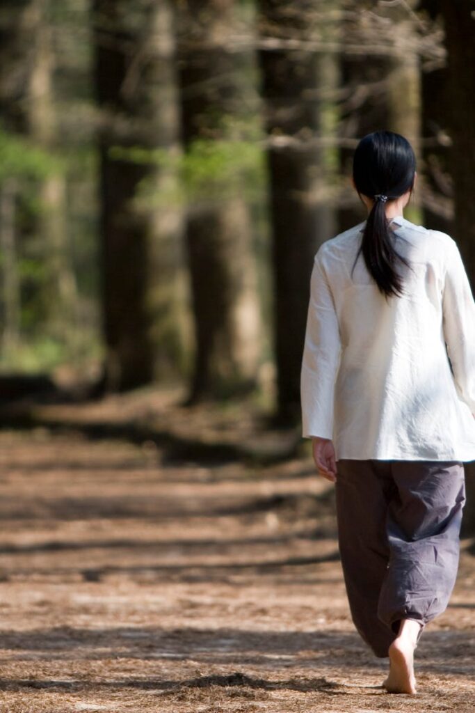 A woman walks barefoot along a peaceful forest path under sunlight, reflecting tranquility.